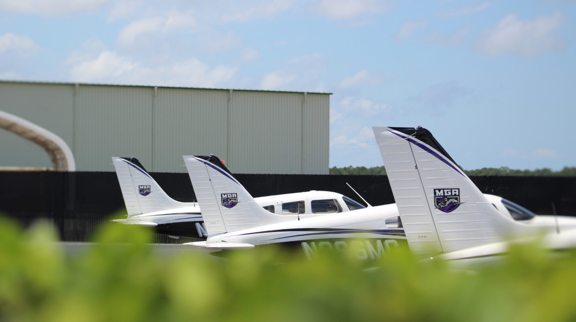 The tail sections of three Piper aircraft parked on an airport apron, bearing the logo of Middle Georgia State University.