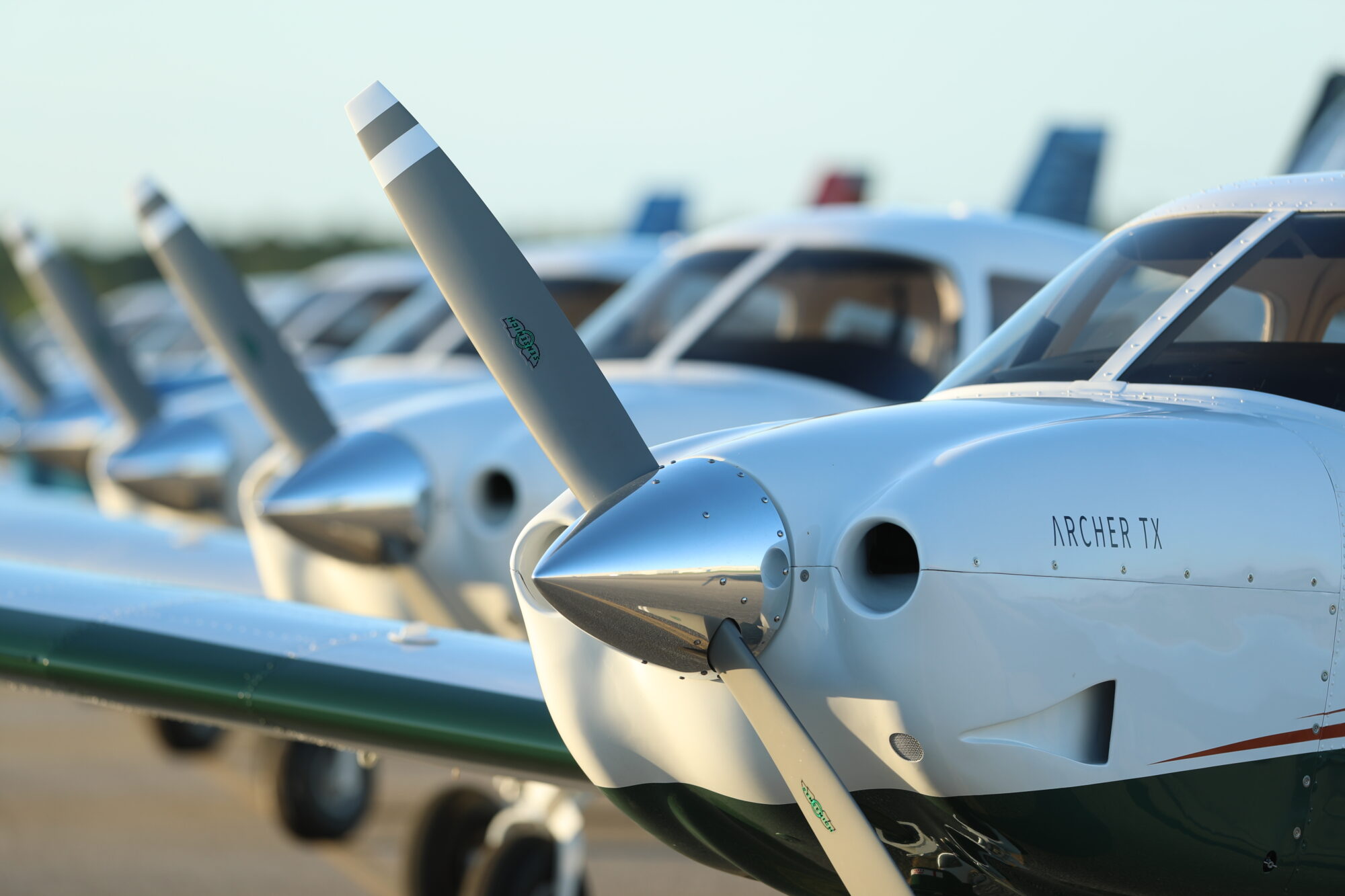 Close-up view of the propeller and nose of a Piper Archer TX with several other training aircraft lined up on the tarmac in the background.