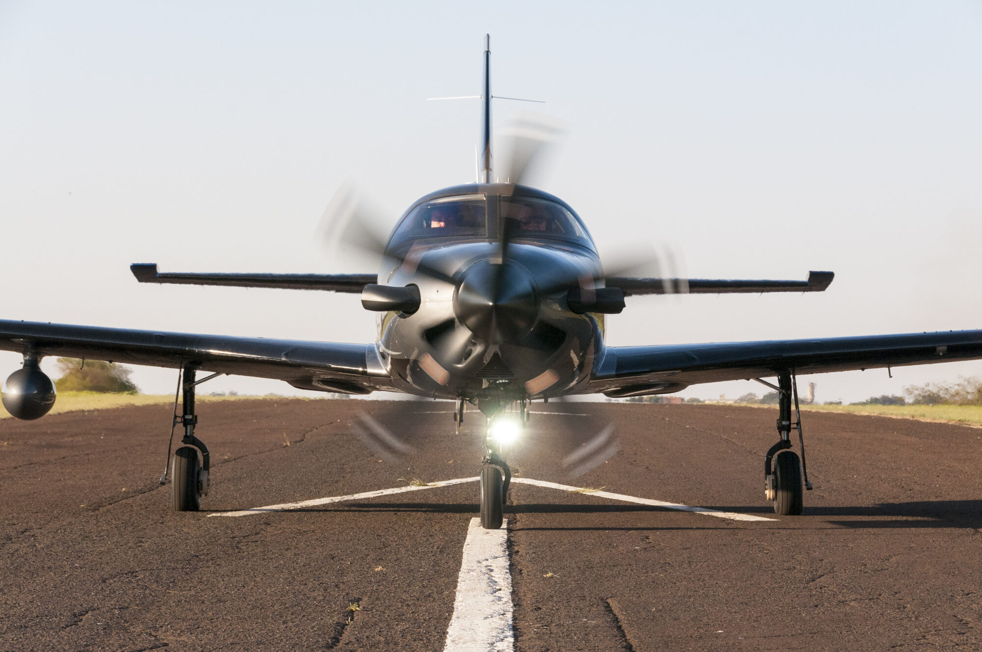 Front view of a Piper Aircraft with its propeller spinning as it prepares for takeoff, with landing gear visible on a runway.